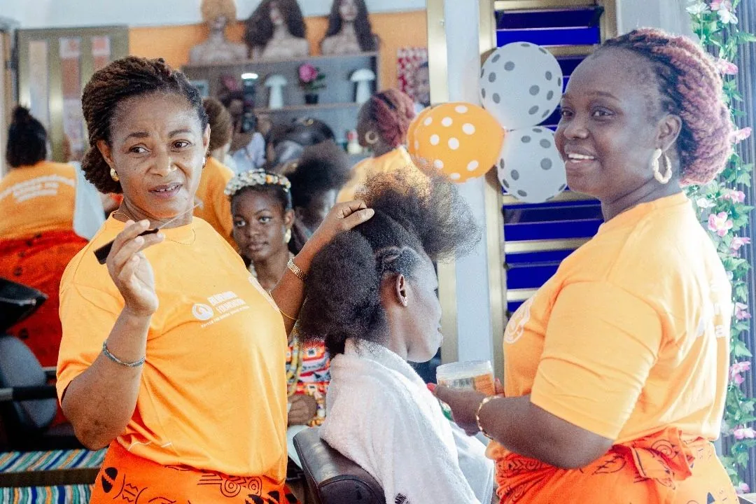 Ambassadrices Heal by Hair en t-shirt orange, dans un salon décoré de ballons, lors d'une session avec une jeune fille.